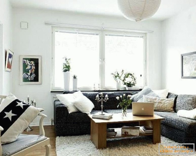 Majhna dnevna soba v beli barvi s temnim kotnim kavčem in oknom