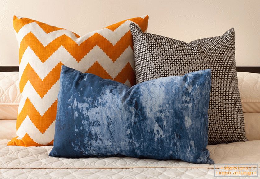 Svetlo oranžne, modre in črno-bele dekorativne blazine z zanimivimi odtisi na postelji