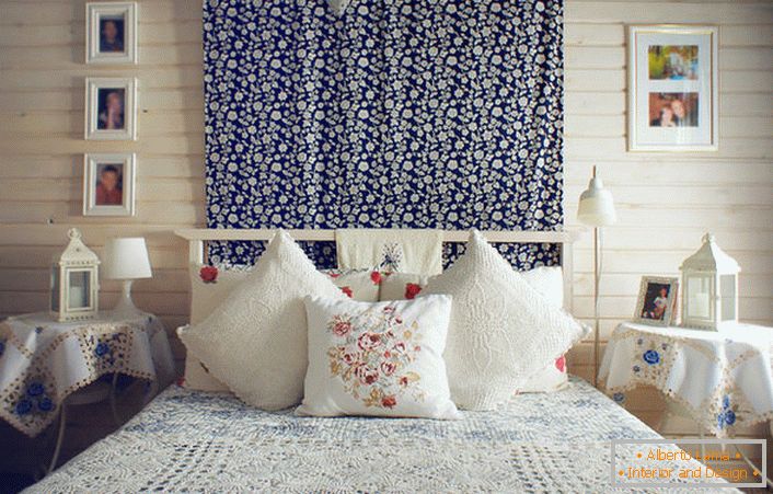 V skladu s kmečkim slogom je postelja okrašena s številnimi blazinami s kontrastnim rdečim vezenjem. Nočne mize so pokrite s prtičkom z občutljivimi modrimi cvetovi.