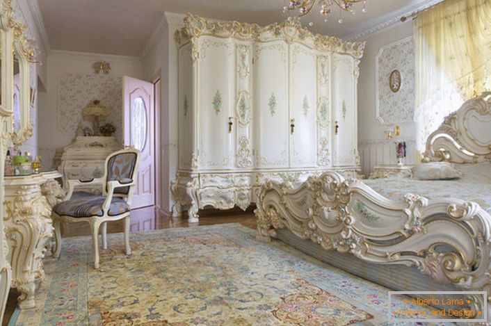 Snežno bela spalnica z izklesanim masivnim pohištvom iz lesa. Postelja z visoko glavo na glavo, elegantno se prilega notranjosti v baročnem slogu.