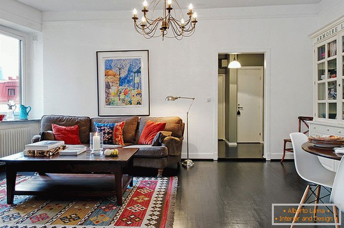 Elegantna soba za goste v tipičnem mestnem stanovanju je okrašena s svetlimi blazinami na kavču in preprogi. 