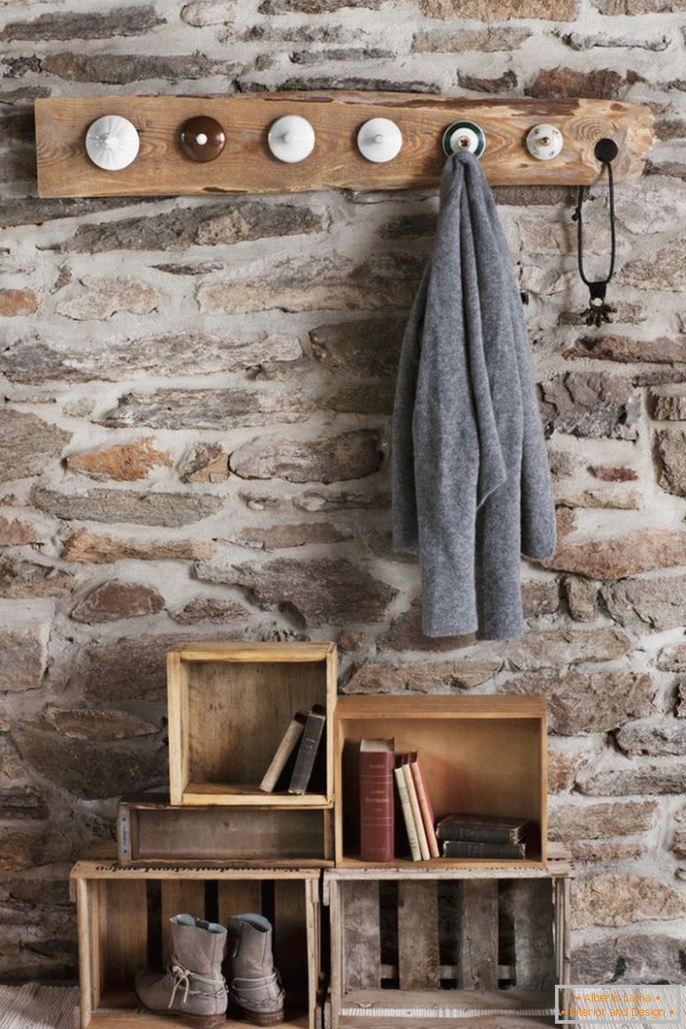Rustic DIY garderoba v sobi s kamnito steno; kljuke iz starih porcelana in stare lesene zaboje na tleh kot skladiščenje