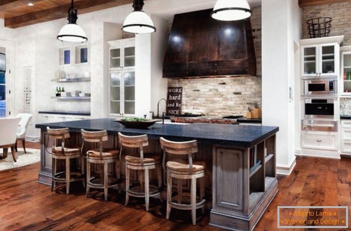 Kuhinja v rustikalnem slogu je razdeljena na delovno in jedilnico. Snežno bela površina harmonizira z dekoracijo temnega lesa in naravnega kamna.