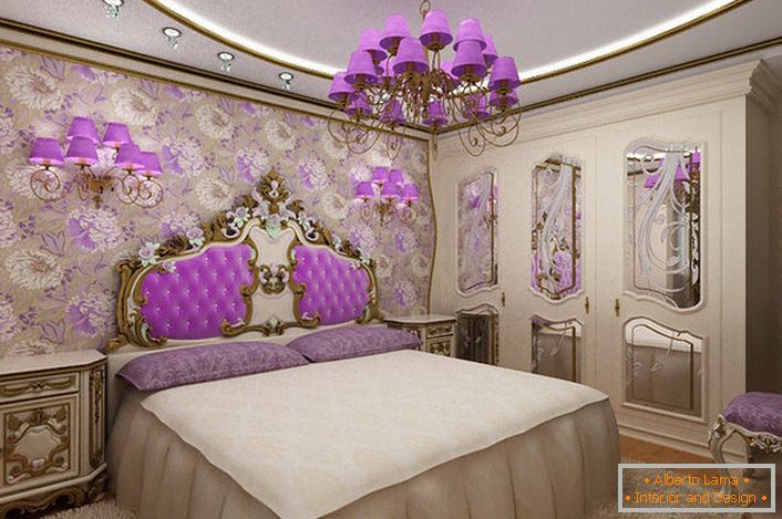 Elegantna baročna spalnica z zanimivim poudarkom na razsvetljavi. Lestenec in nočne svetilke z enakimi vijoličnimi odtenki, ki so harmonično povezani z oblazinjenjem naslonjala na glavi postelje.